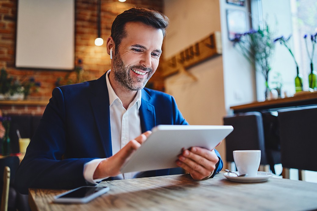Man wearing earbuds using tablet in coffee shop