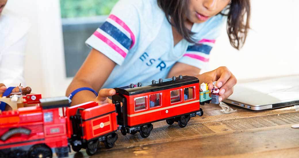 A child with long hair plays excitedly with a red toy train.